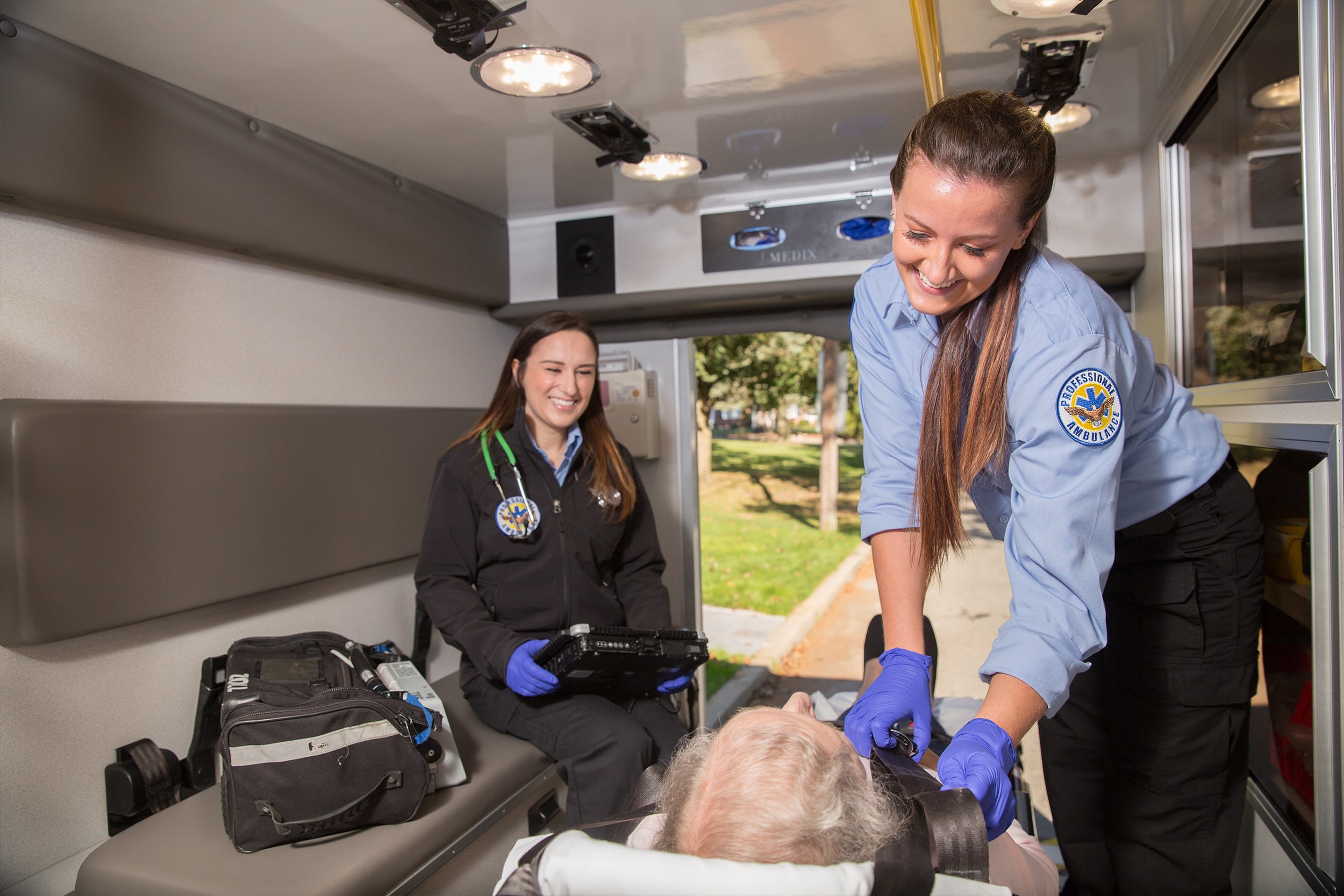 Two female EMTs helping elderly in Ambulance